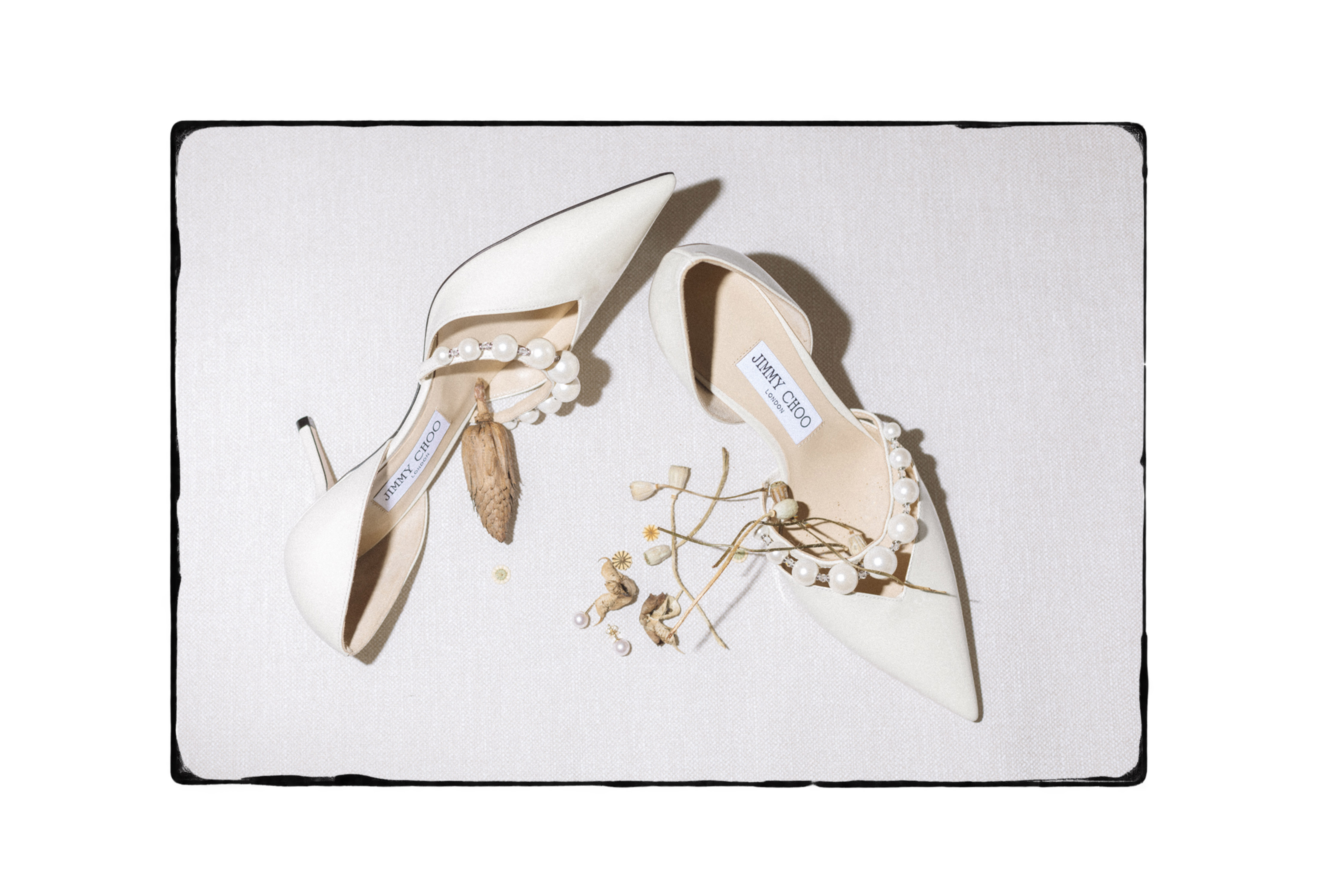Weiße Brautschuhe mit Perlendetail und getrockneten Blüten auf hellem Untergrund