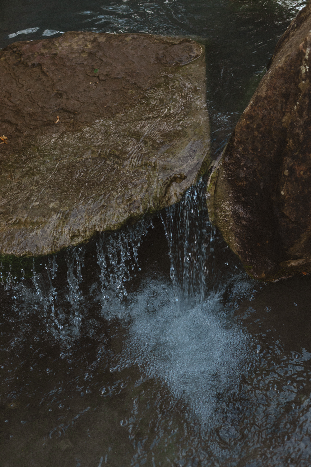 Wasser fällt zwischen zwei Felsen in ein dunkles Becken